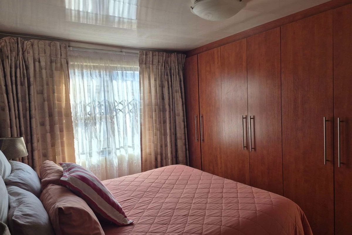 A bedroom featuring extensive built-in wooden cupboards, a glossy ceiling finish, and a window fitted with a security gate.