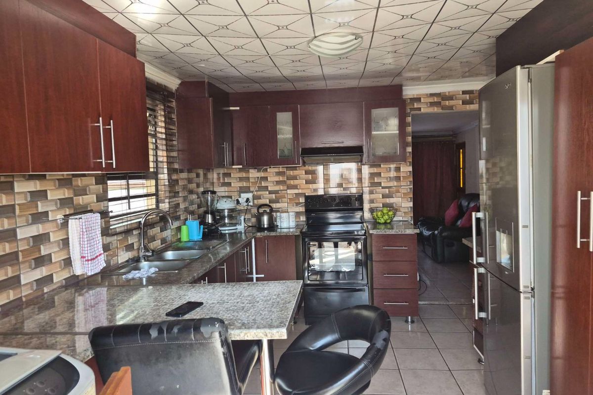 A functional kitchen featuring dark wood cabinetry, granite countertops, a tiled backsplash, and a freestanding stove, with direct access to the adjacent living area.