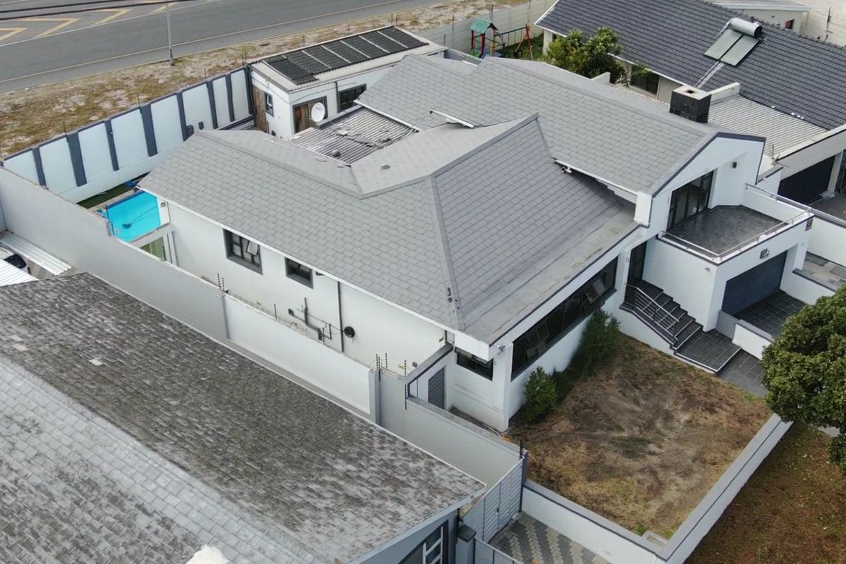 Aerial view of a modern residential property featuring a tiled roof with solar panels, a swimming pool, and secure perimeter walling.