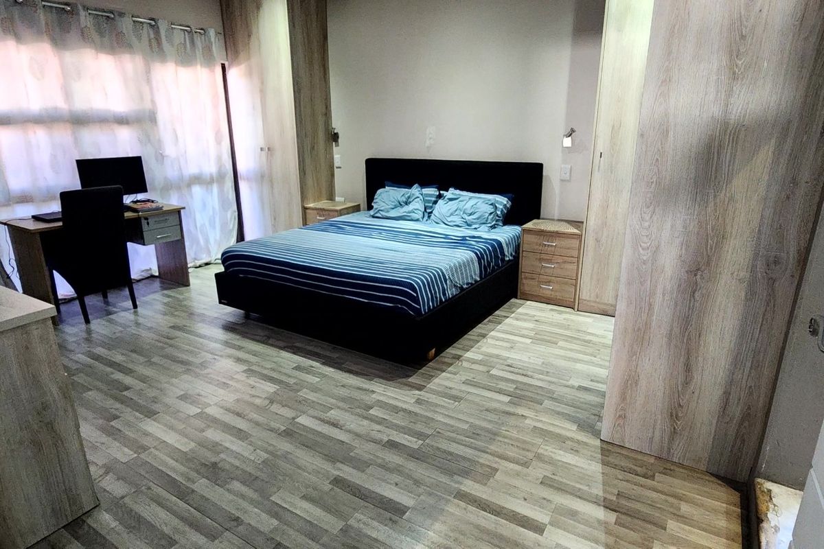 A well-maintained bedroom featuring modern laminate flooring, built-in wooden cupboards, and neutral wall finishes.