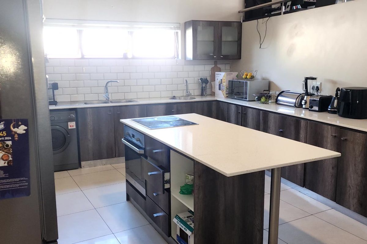 Modern kitchen featuring dark wood-finish cabinetry, white quartz countertops, a central island with integrated cooktop and oven, and a classic subway tile backsplash.