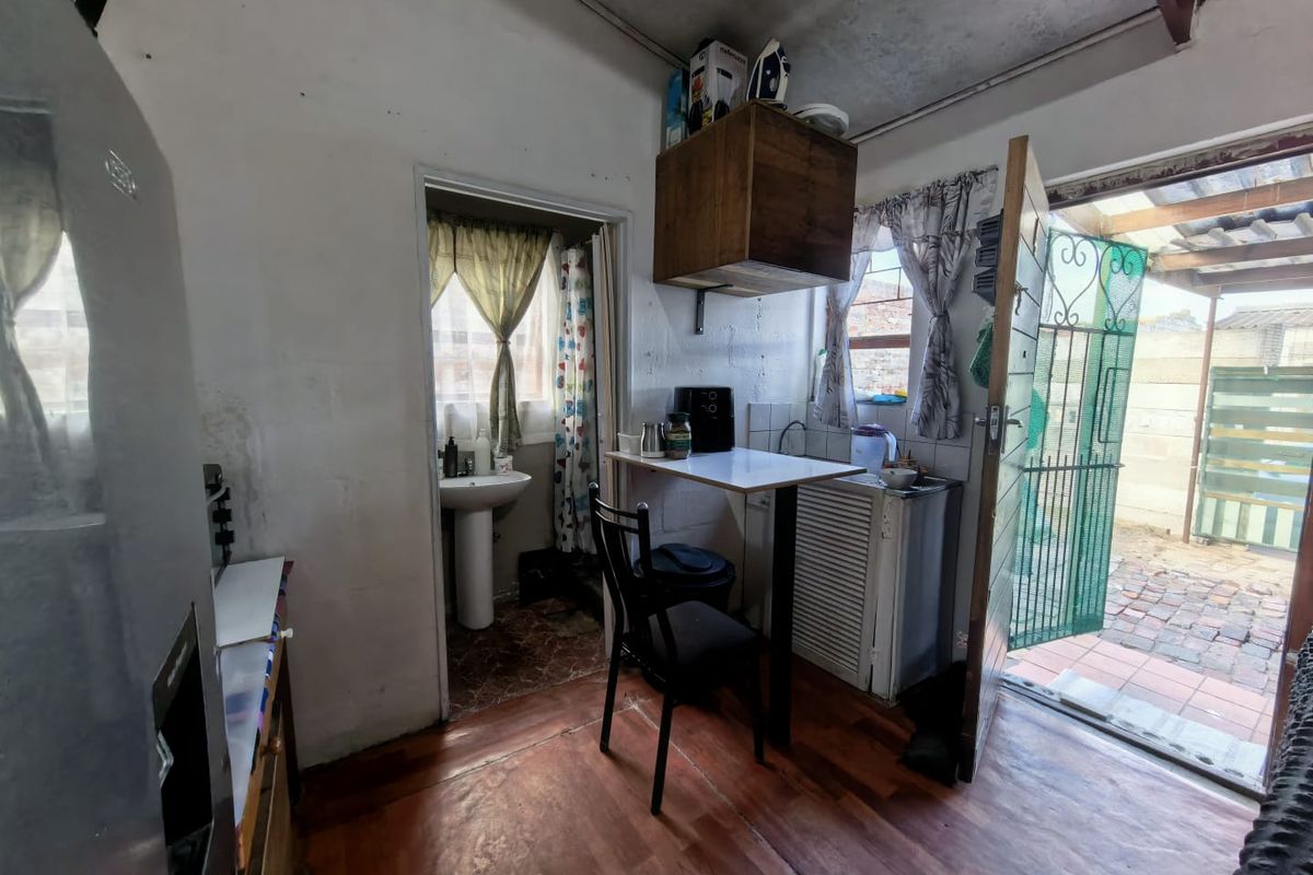 A compact kitchen area featuring timber flooring, a pedestal sink in the adjacent space, and direct access to an outdoor patio area.