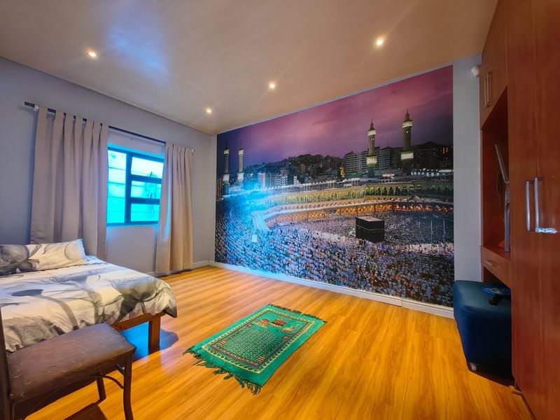 A well-maintained bedroom featuring laminate flooring, recessed downlighting, and a built-in wardrobe, with a large feature wall mural.