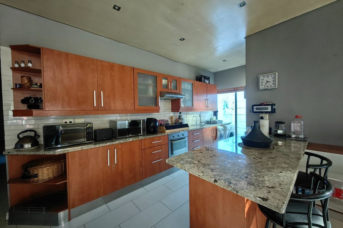 A functional kitchen featuring wooden cabinetry, granite countertops, a breakfast bar, and built-in appliances, with tiled flooring and recessed ceiling lighting.