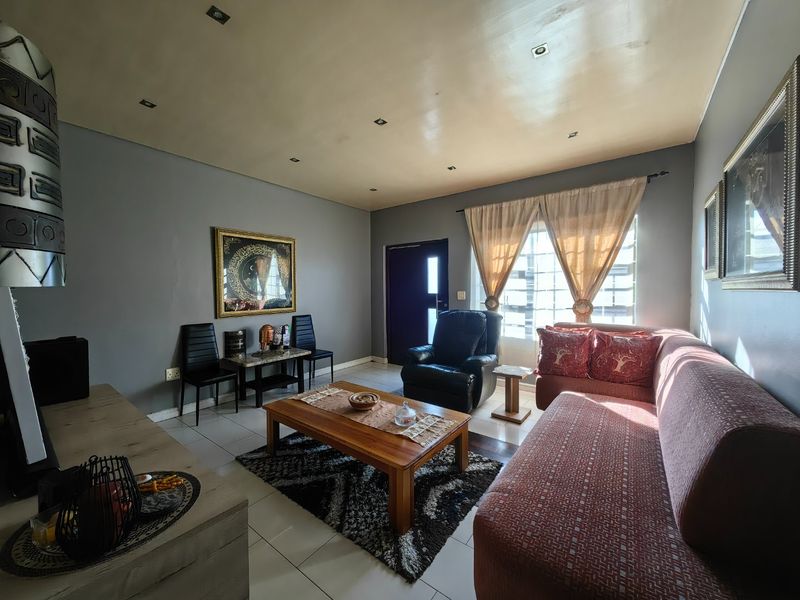 A comfortable living room featuring tiled flooring, recessed downlighting, and a window fitted with security burglar bars.