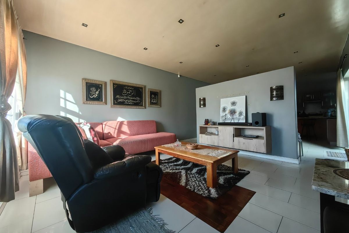 A living room featuring tiled flooring, recessed downlights, and a partition wall separating the space from the kitchen area.