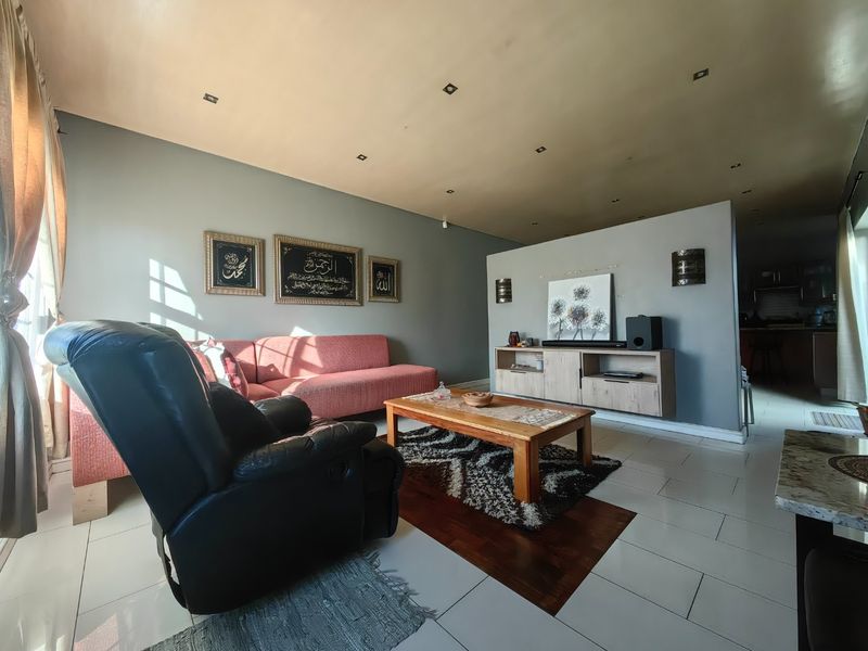 A living room featuring tiled flooring, recessed downlights, and a partition wall separating the space from the kitchen area.