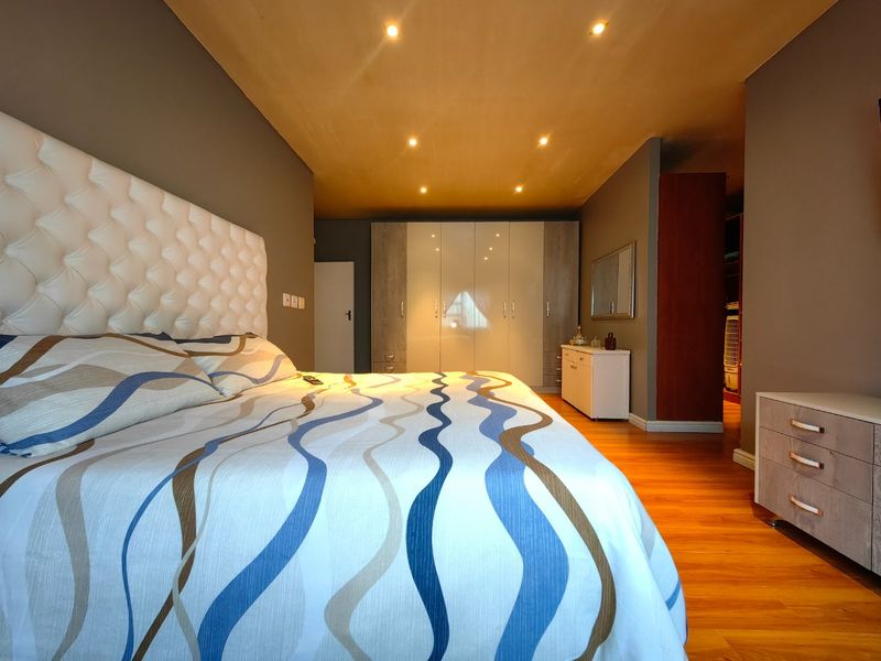 Spacious bedroom featuring modern built-in wardrobes, warm laminate flooring, and recessed downlighting, creating a comfortable and well-maintained living space.