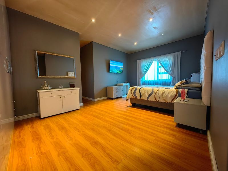 Spacious bedroom featuring warm-toned laminate flooring, recessed downlighting, and dark grey feature walls, offering a comfortable and functional living space.
