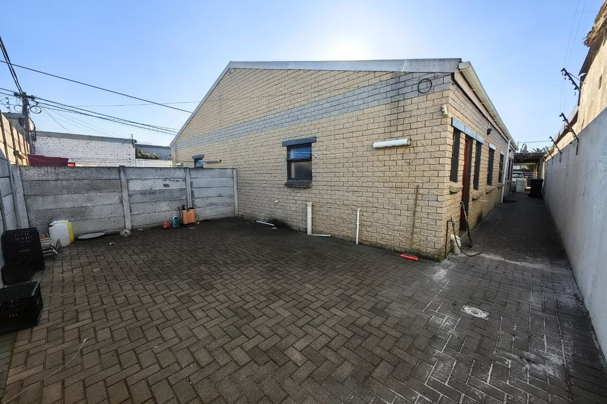Rear exterior view of the property featuring a paved courtyard area, face brick facade, and precast concrete boundary walling.