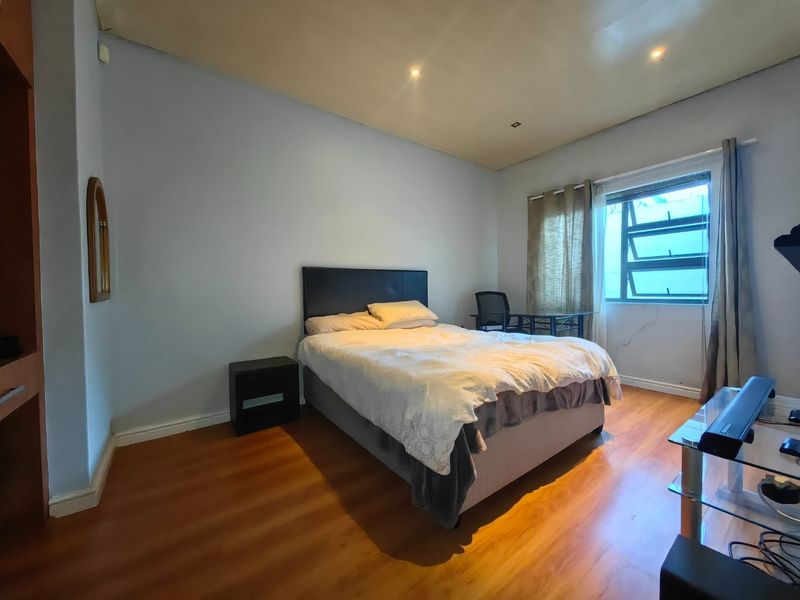 A bedroom featuring laminate flooring, recessed downlighting, and an aluminium window frame. Visible plaster cracking is present beneath the window.