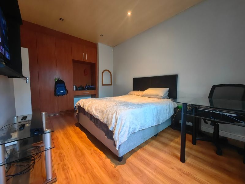 A bedroom featuring laminate flooring, built-in wooden cupboards with a vanity nook, and recessed ceiling lighting.