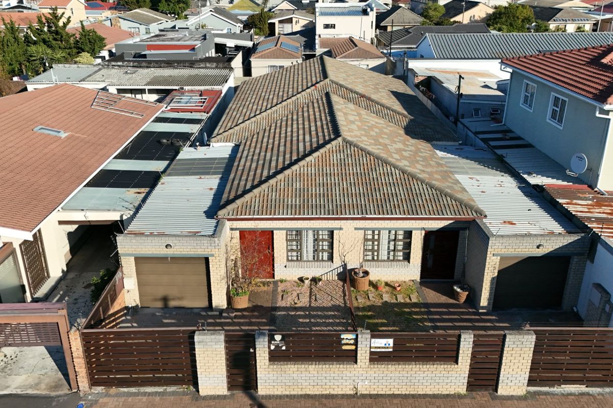 Aerial view of a residential property featuring a tiled roof, brick facade, dual garages, and a secure perimeter wall with gated access.