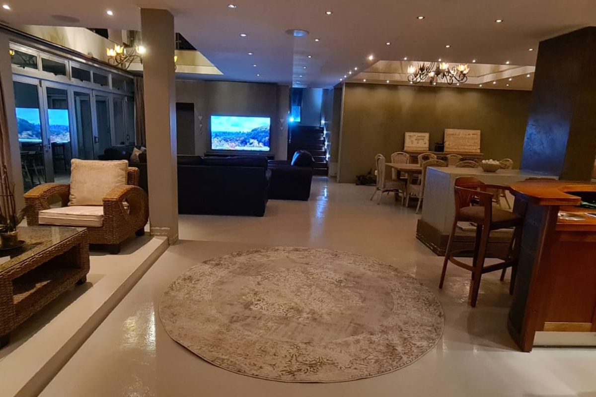 Spacious open-plan living area featuring polished concrete floors, a built-in bar, recessed lighting, and seamless flow to the outdoor patio through sliding glass doors.