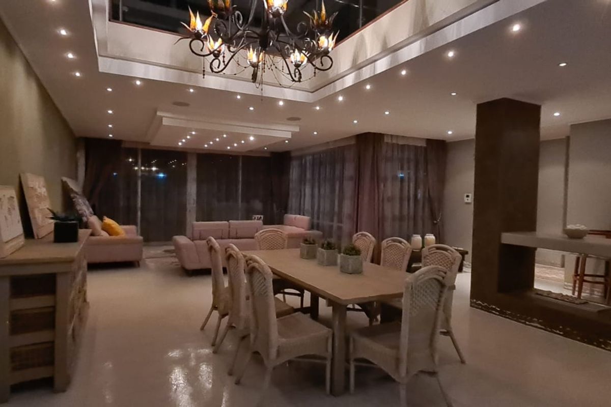 Spacious open-plan living and dining area featuring a coffered ceiling with recessed lighting, a central fireplace, and a built-in bar area.