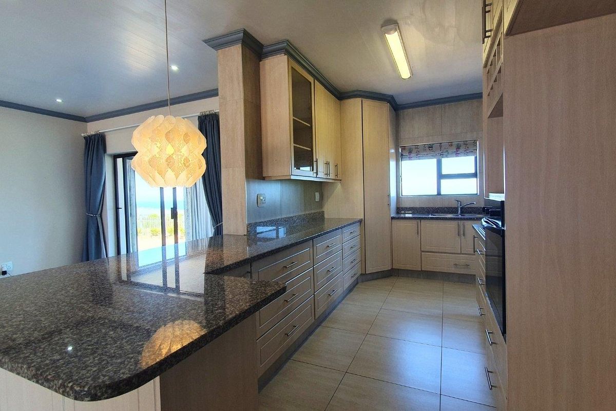 A well-appointed kitchen featuring granite countertops, extensive built-in cabinetry, a built-in oven, and tiled flooring, with an open-plan layout leading to a living area.