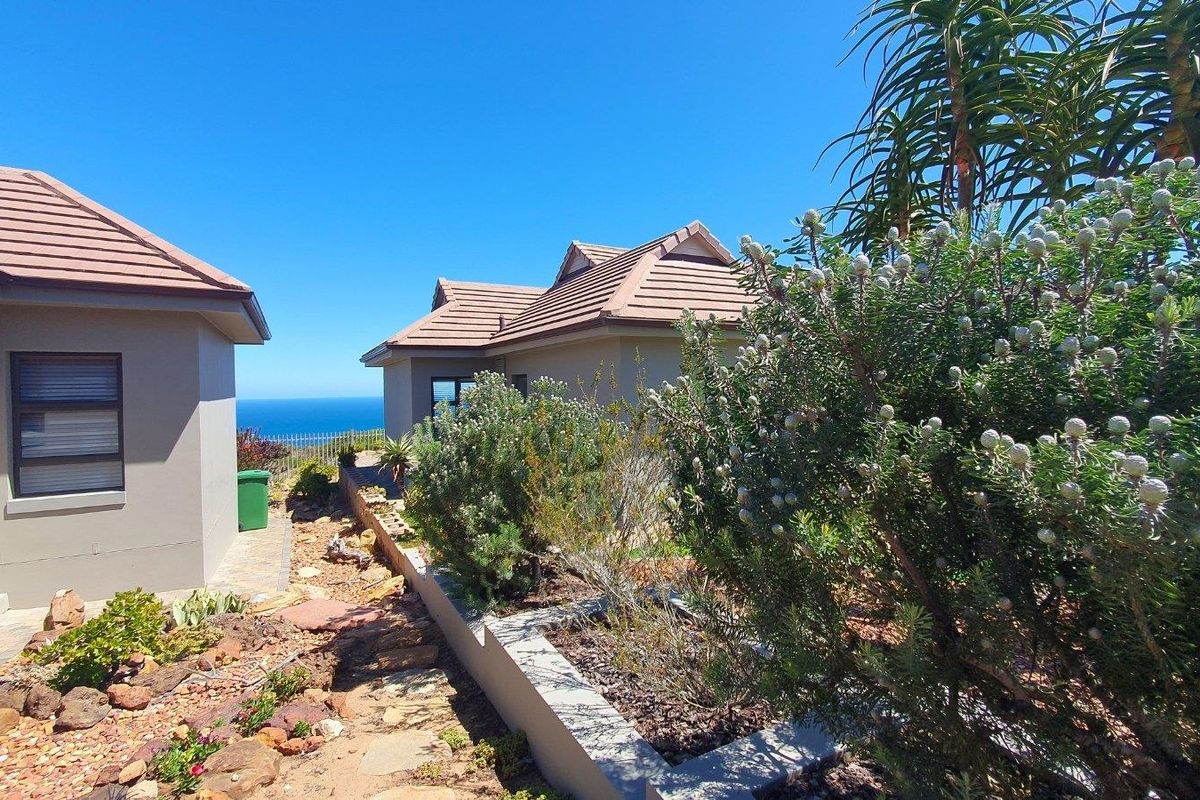 Rear exterior view of the property featuring a landscaped garden, paved pathways, and a clear view of the ocean in the distance.