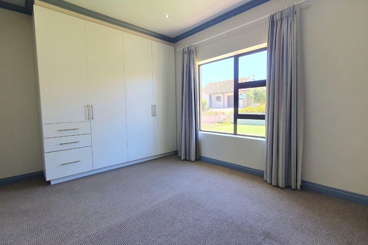 A bright, empty bedroom featuring neutral carpeting, built-in cupboards, and a large window with views of the exterior.