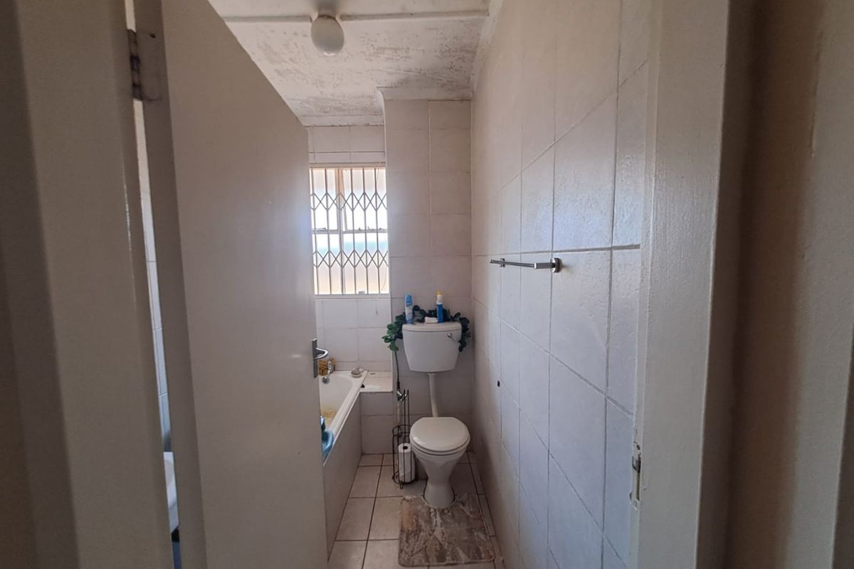 A dated bathroom featuring a bathtub, toilet, and tiled finishes, currently showing significant signs of wear and ceiling deterioration requiring maintenance.