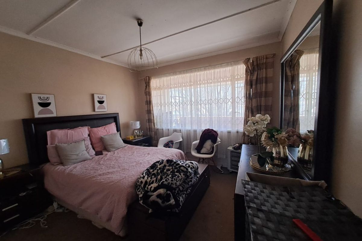 A bedroom featuring a large window with security gate, curtain rails, and a central pendant light fitting.