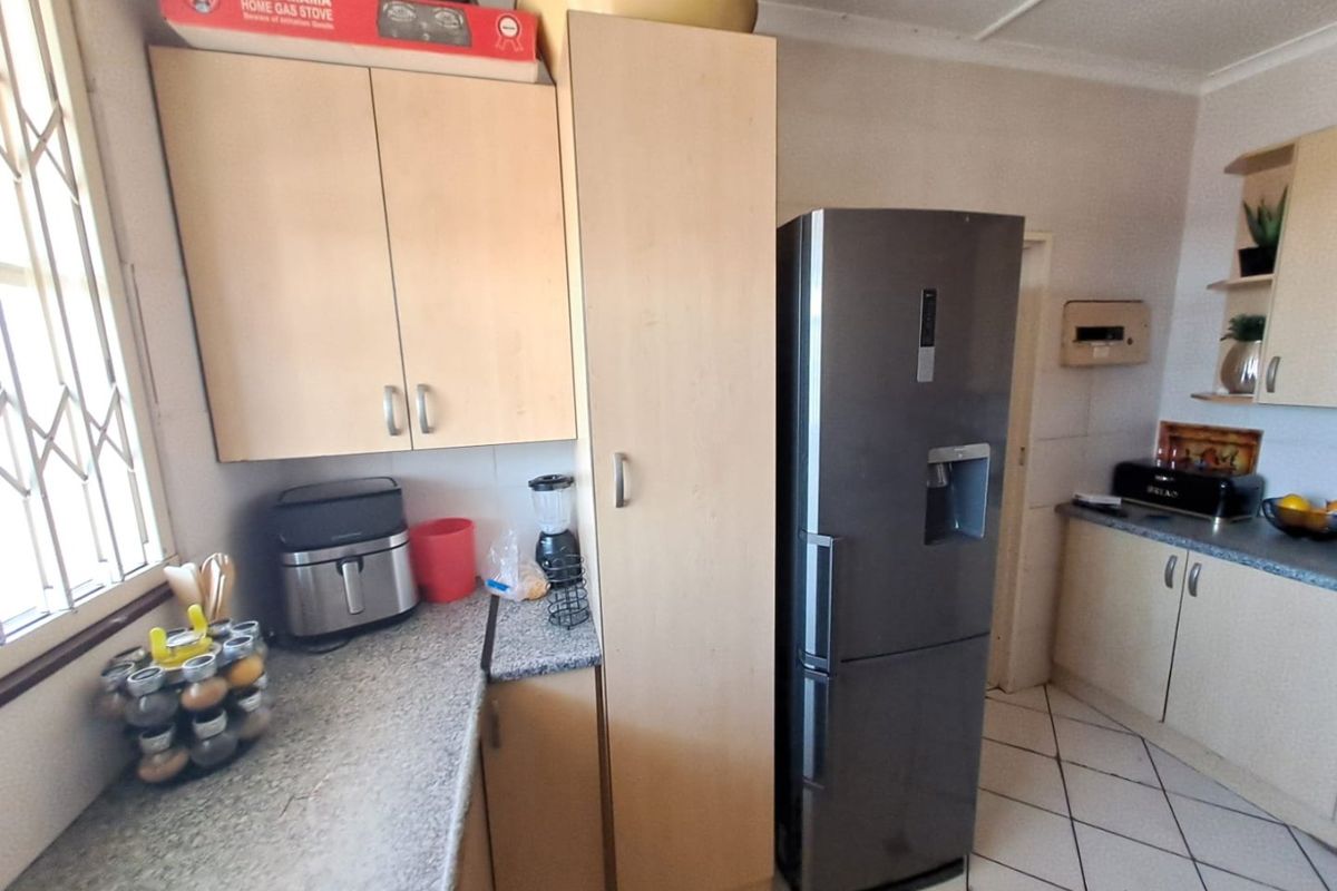 A functional kitchen featuring laminate cabinetry, granite-look countertops, and ceramic floor tiles, providing a practical workspace with natural light from the side window.