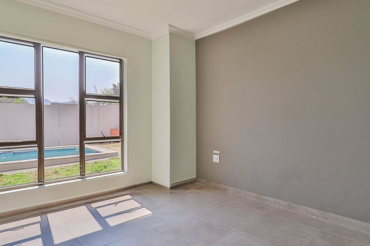 A bright, empty living area featuring neutral wall tones, tiled flooring, and large windows providing a view of the outdoor pool area.