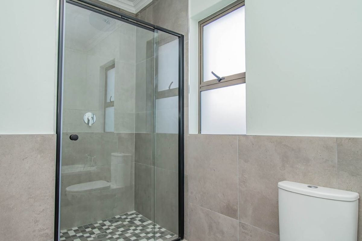 Modern bathroom featuring a glass-enclosed shower, neutral wall tiling, and a clean, minimalist design with a frosted window for privacy.