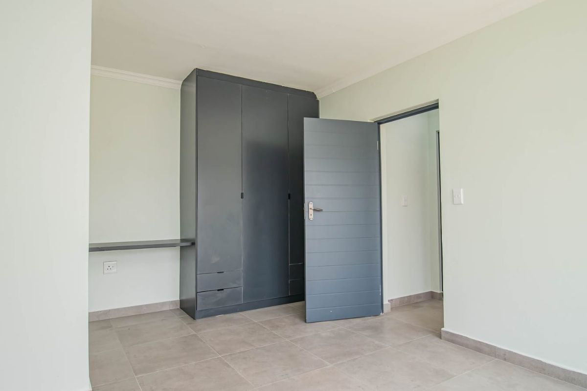 A clean, neutral bedroom featuring modern grey built-in cabinetry, tiled flooring, and a contemporary internal door.