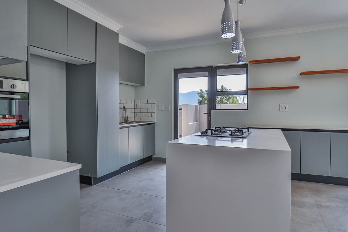 Modern kitchen featuring a central island with gas hob, sleek grey cabinetry, quartz countertops, subway tile backsplash, and integrated oven.