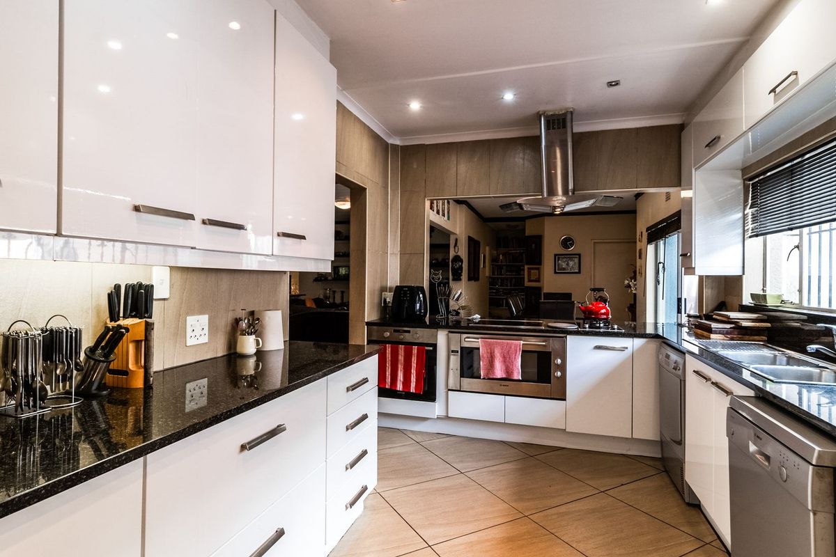 Modern kitchen featuring high-gloss white cabinetry, granite countertops, stainless steel appliances, and tiled flooring with integrated lighting.