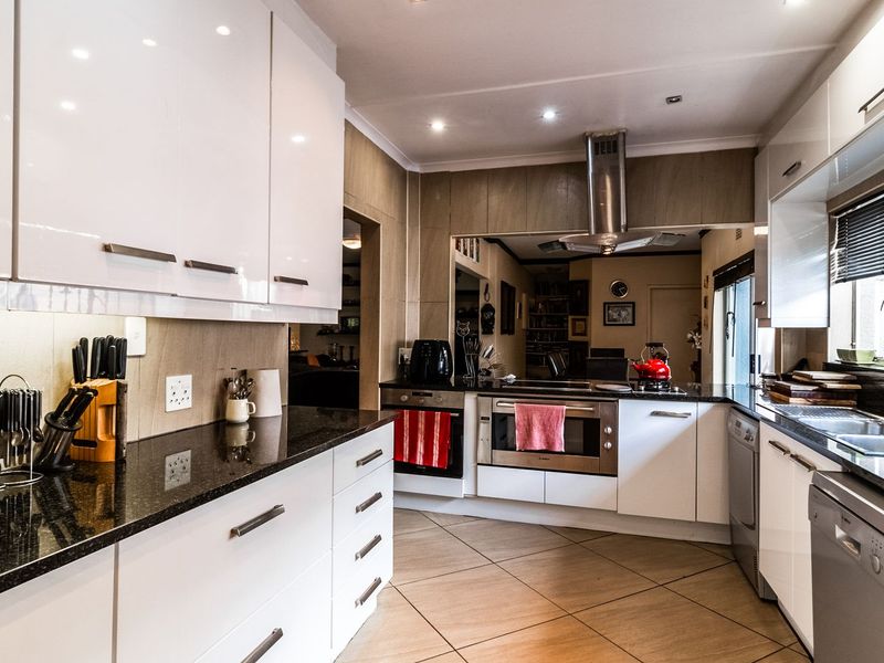 Modern kitchen featuring high-gloss white cabinetry, granite countertops, stainless steel appliances, and tiled flooring with integrated lighting.