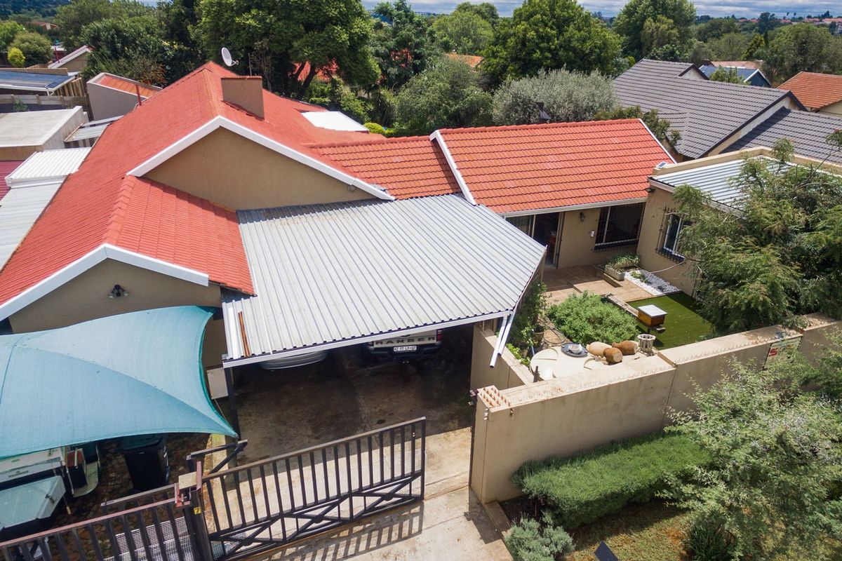 Aerial view of the property showing the tiled roof, corrugated metal carport, paved driveway, and perimeter wall with a sliding gate.