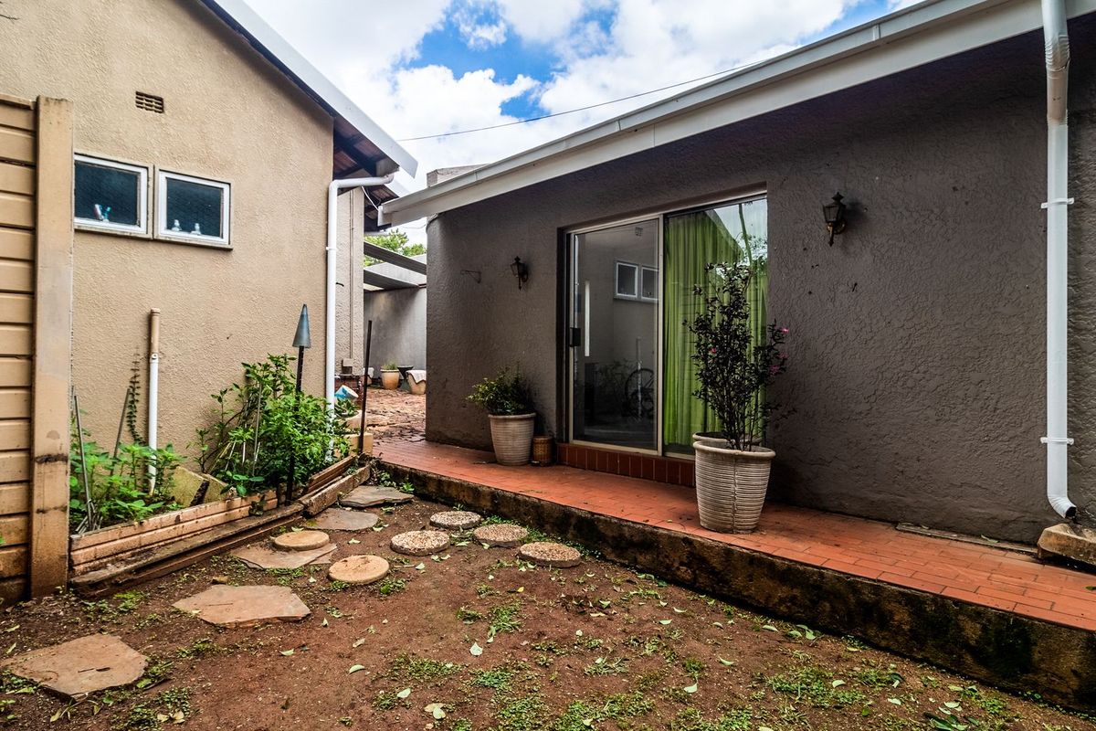 A rear exterior view showing a paved walkway, sliding door access, and a small garden area between two building structures.