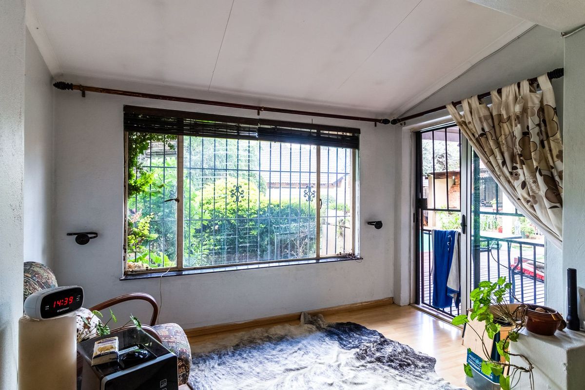 A living room featuring laminate flooring, security bars on the window, and a sliding glass door providing access to the outdoor area.