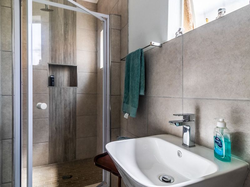 A modern bathroom featuring a tiled shower enclosure with a built-in niche and a wall-mounted basin with a chrome mixer tap.
