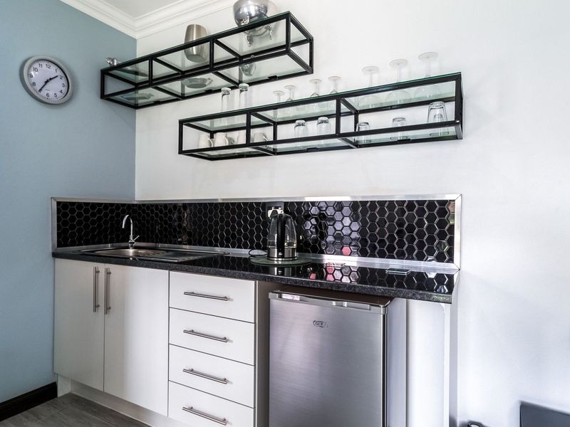 A compact scullery or kitchenette area featuring modern white cabinetry, a black hexagonal tile backsplash, granite countertops, and stylish wall-mounted glass shelving.