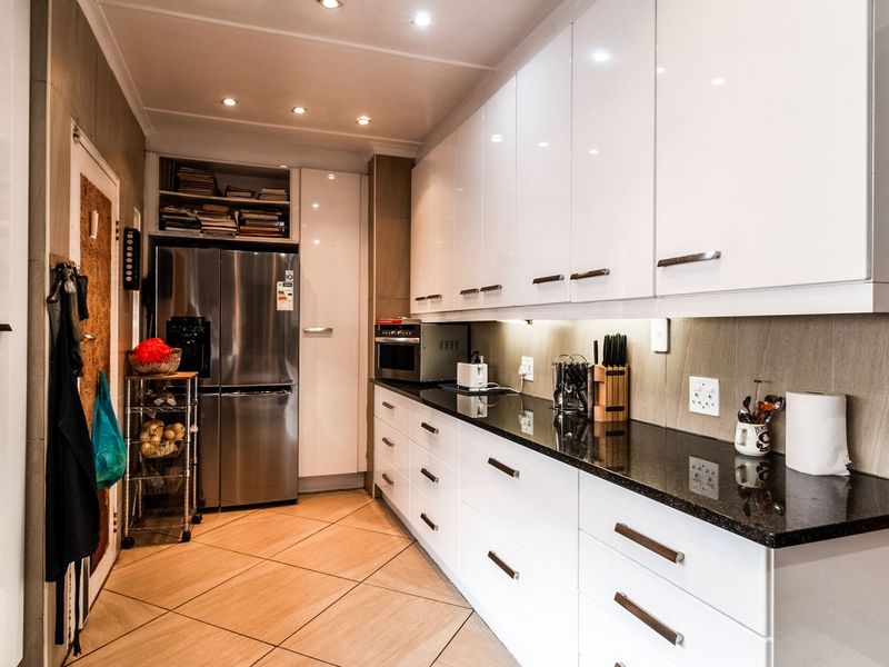 Modern kitchen featuring sleek white cabinetry, dark granite countertops, recessed lighting, and tiled flooring, offering a clean and functional workspace.