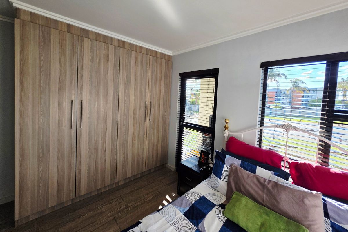A well-maintained bedroom featuring modern wood-grain built-in cupboards, laminate flooring, and venetian blinds, offering a clean and functional living space.