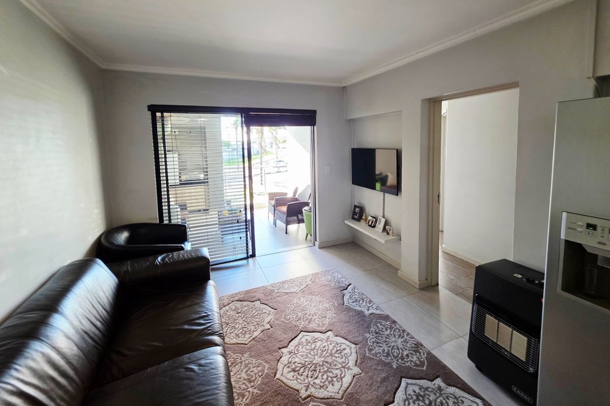 A living room featuring tiled flooring, a wall-mounted shelf, and a sliding glass door providing access to an outdoor balcony area.