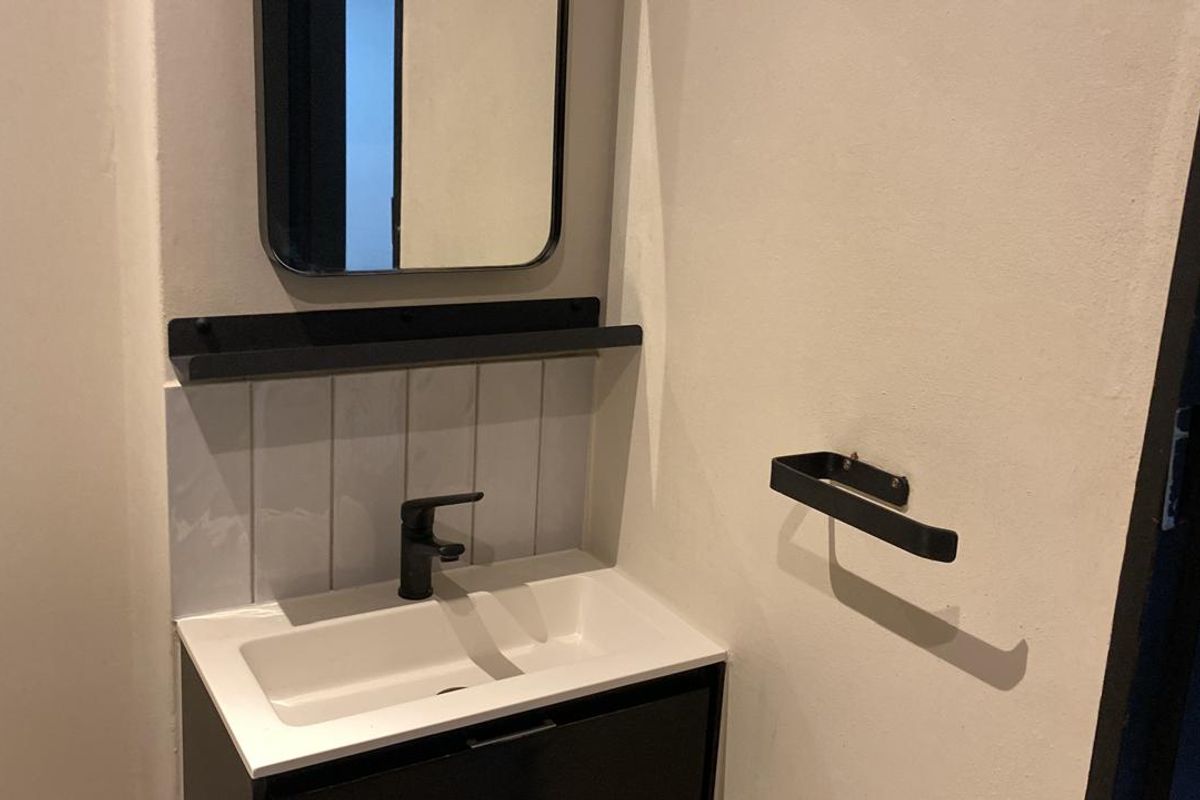 A modern bathroom vanity area featuring a sleek black cabinet, integrated basin, wall-mounted tap, and minimalist black fixtures.