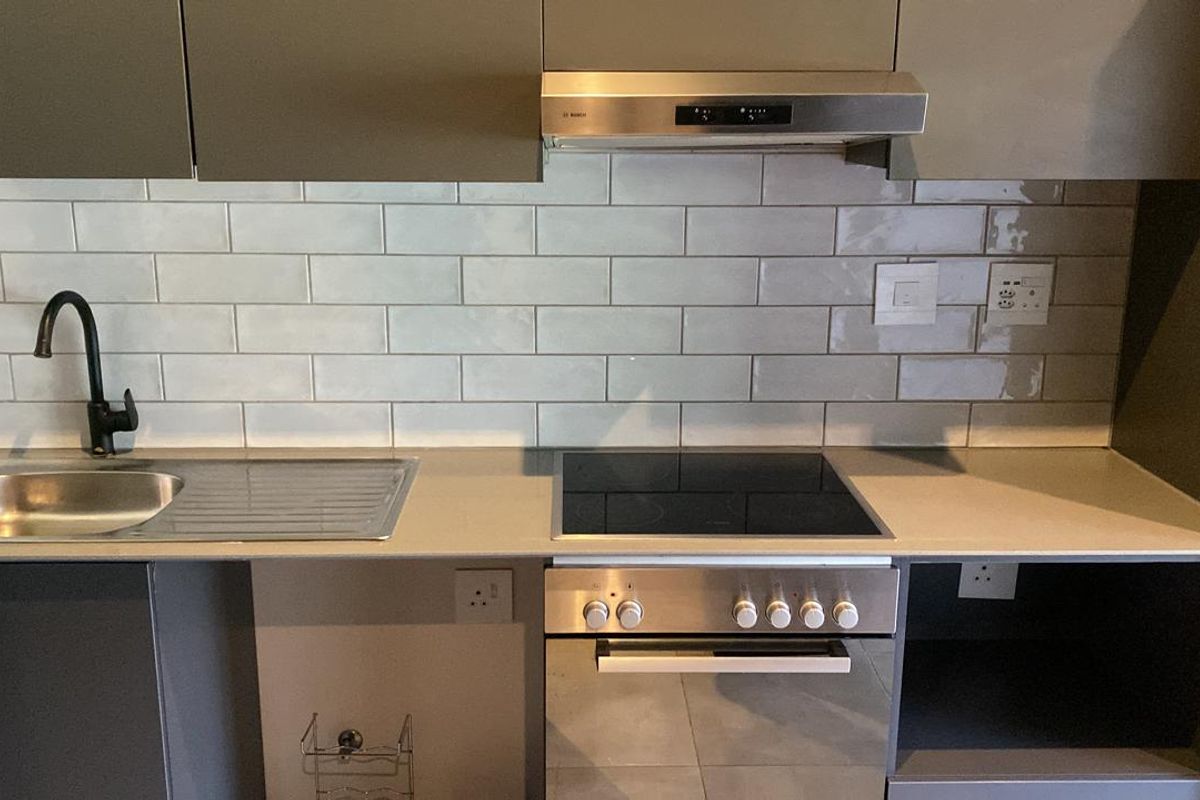 Modern kitchen featuring a subway tile backsplash, stone countertops, integrated electric cooktop, oven, and extractor fan with a sleek stainless steel sink.