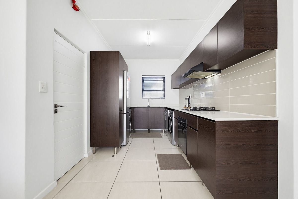 Modern galley-style kitchen featuring dark wood cabinetry, stone countertops, tiled backsplash, built-in oven, gas hob, and integrated extractor fan.