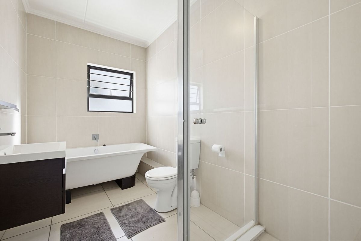 A clean, modern bathroom featuring a freestanding bathtub, a separate glass-enclosed shower, and neutral floor-to-ceiling tiling.