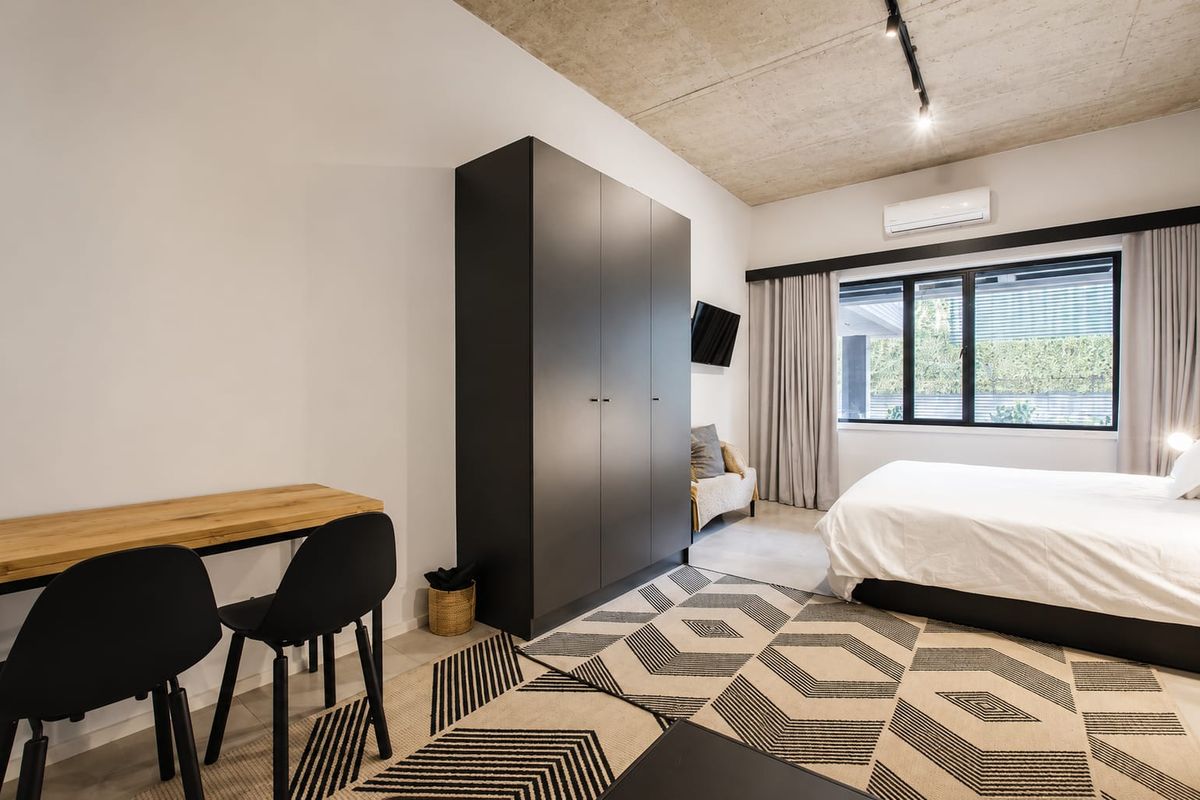 Modern bedroom featuring an exposed concrete ceiling, built-in wardrobe, split-system air conditioning, and large windows providing natural light.