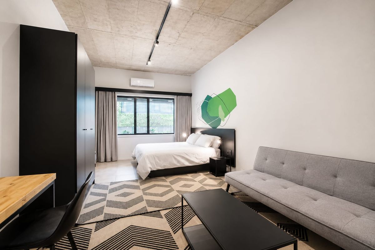 Modern bedroom featuring an exposed concrete ceiling, track lighting, split-system air conditioning, and a built-in wardrobe with a neutral aesthetic.