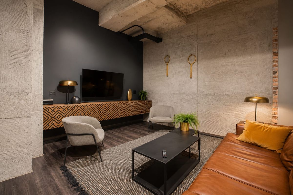 Modern living room featuring industrial-style exposed concrete walls and ceiling, complemented by dark laminate flooring and custom built-in wall cabinetry.