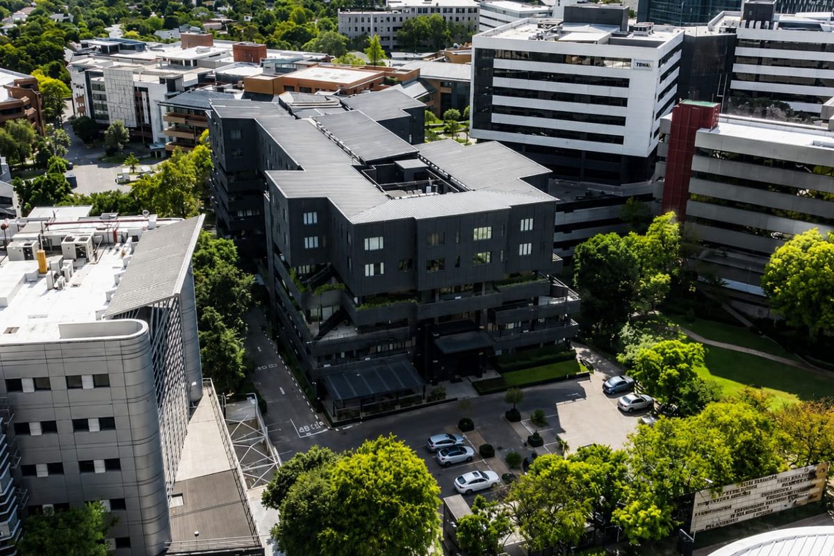 Aerial view of a modern multi-story apartment complex featuring a dark facade, surrounding landscaped grounds, and an on-site parking area.