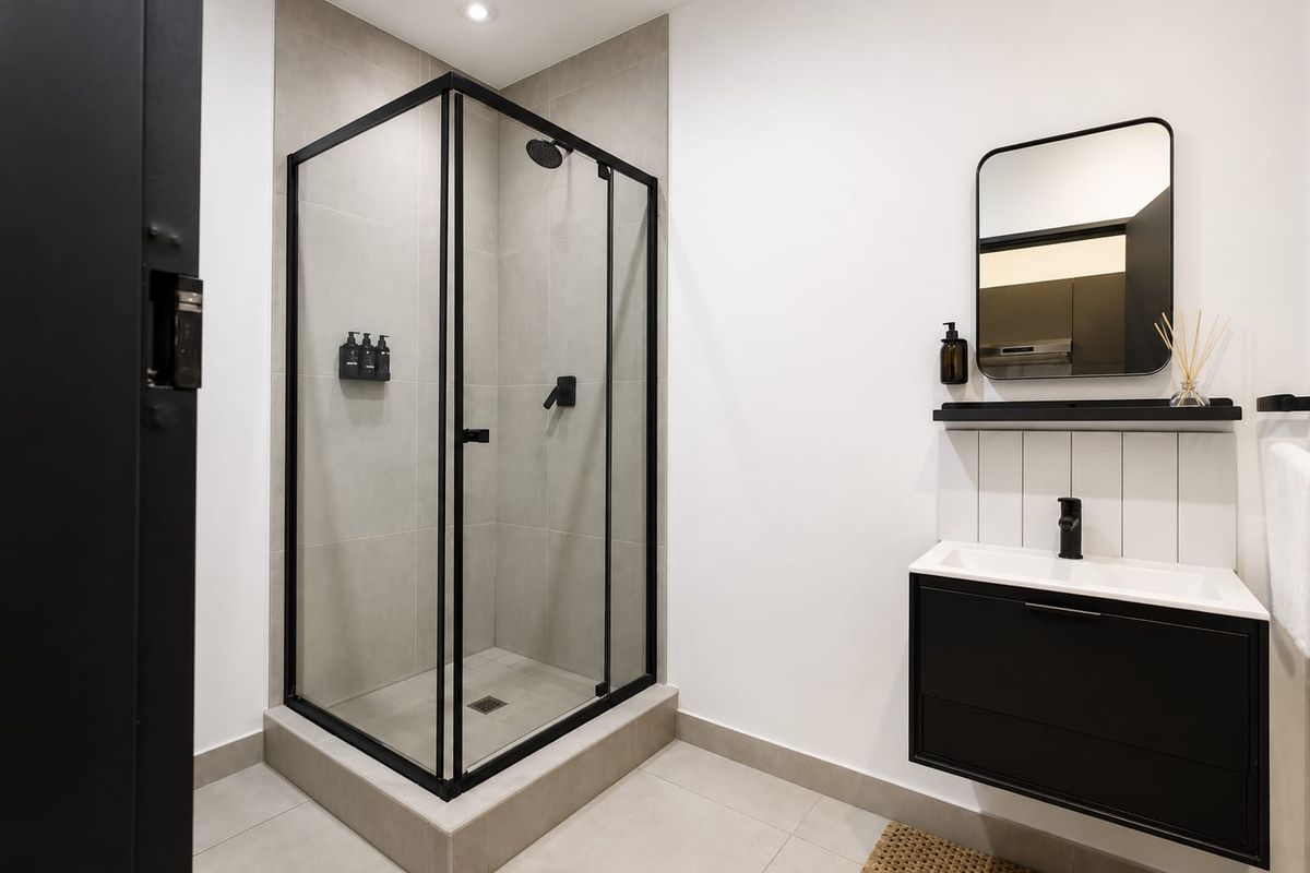 Modern bathroom featuring a sleek black-framed shower enclosure, wall-mounted vanity with integrated basin, and contemporary matte black fixtures.