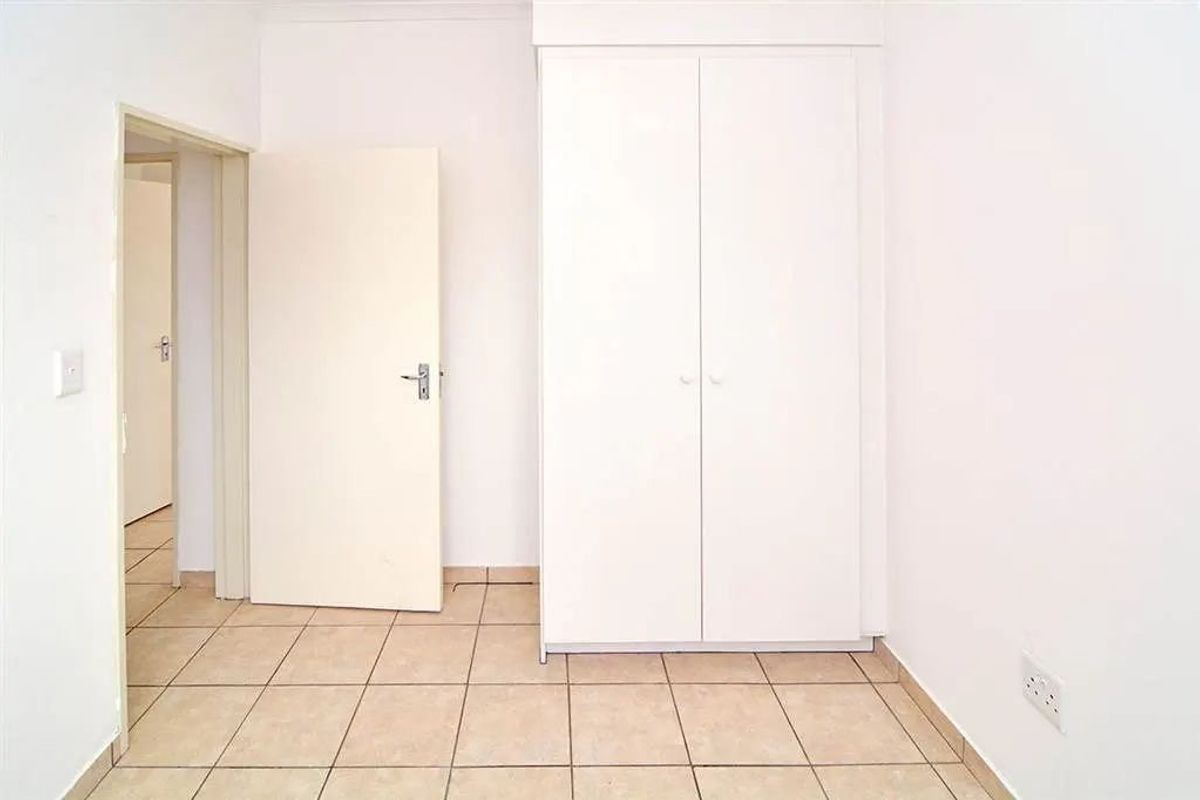 A clean, empty bedroom featuring neutral tiled flooring and a built-in white wardrobe, offering a blank canvas for personalization.