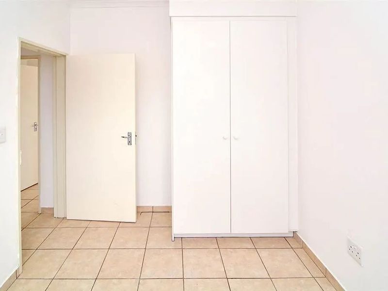 A clean, empty bedroom featuring neutral tiled flooring and a built-in white wardrobe, offering a blank canvas for personalization.